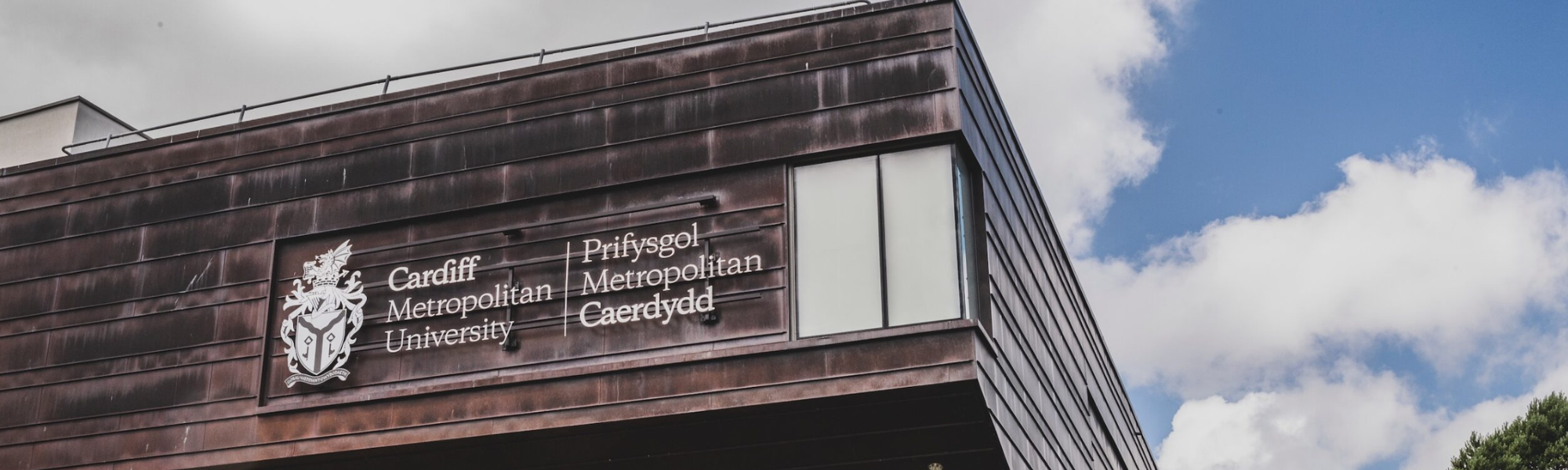 Cardiff Metropolitan University logo on building with sky background