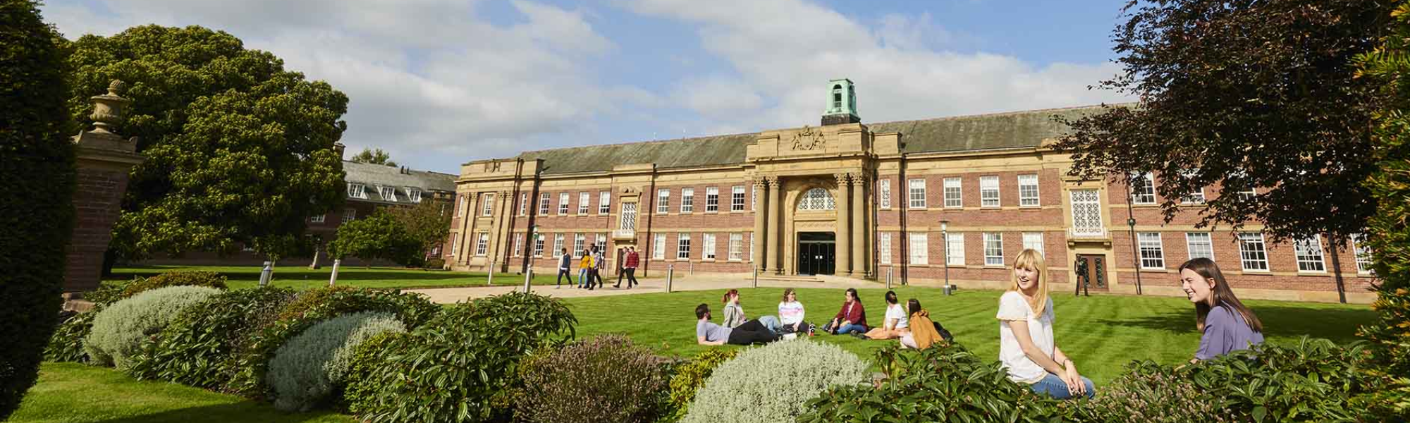 Edge Hill University with greenery and students sitting on the lawn 